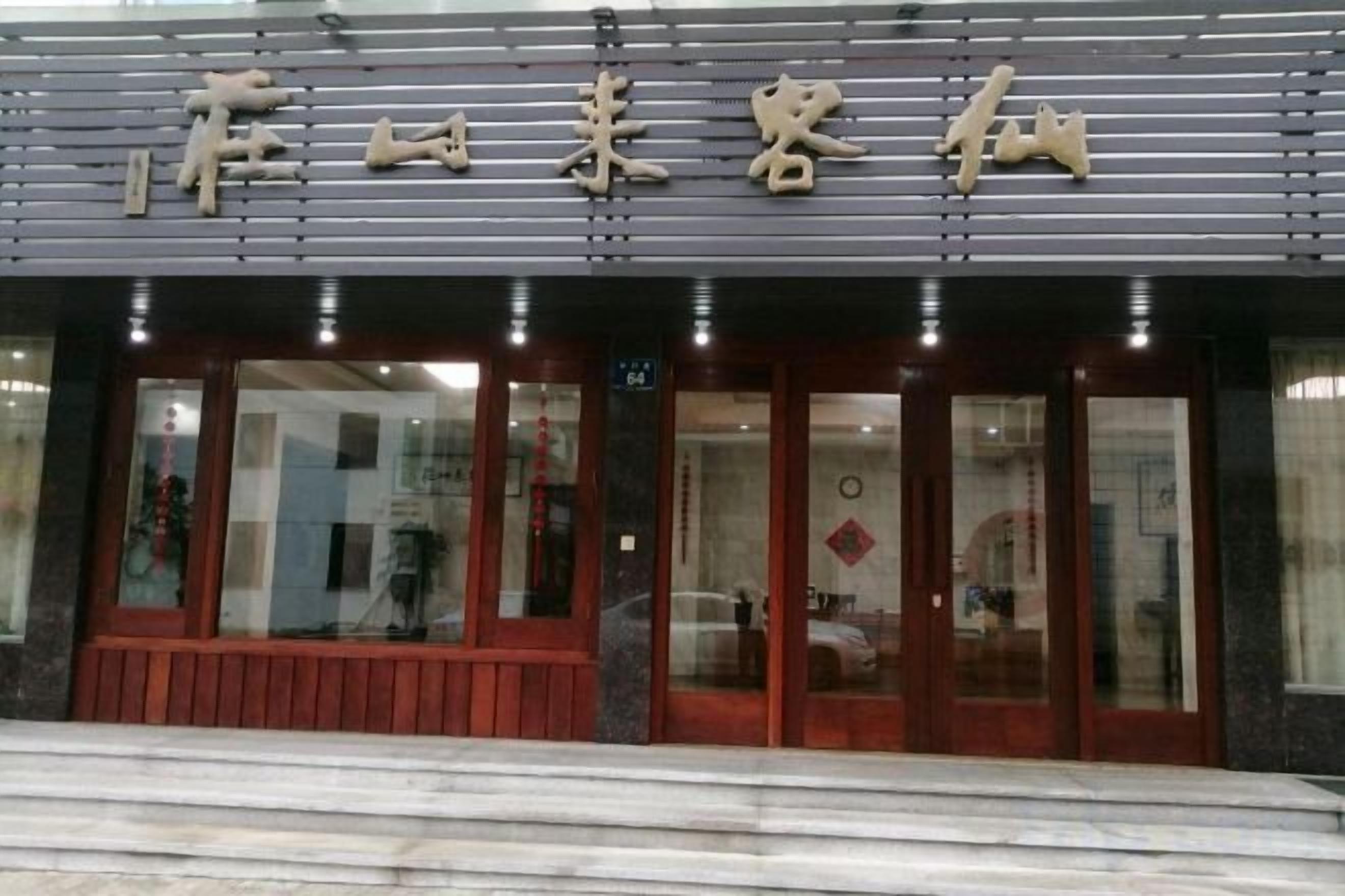 A hotel entrance with a sign above the doors, a bench outside, and a reflection in the glass.