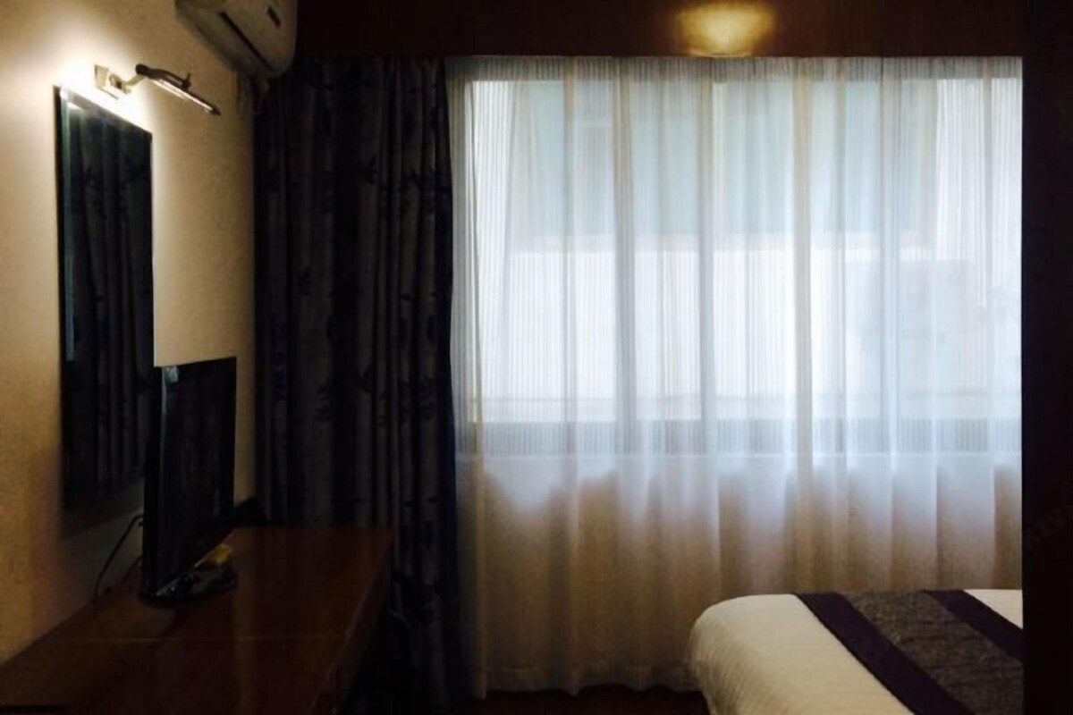 Una habitación de hotel con una cama, un escritorio con lámpara, un espejo y cortinas translúcidas.