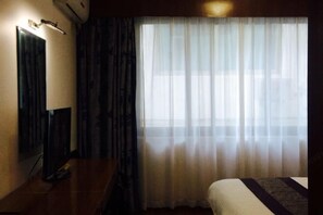 Una habitación de hotel con una cama, un escritorio con lámpara, un espejo y cortinas translúcidas.