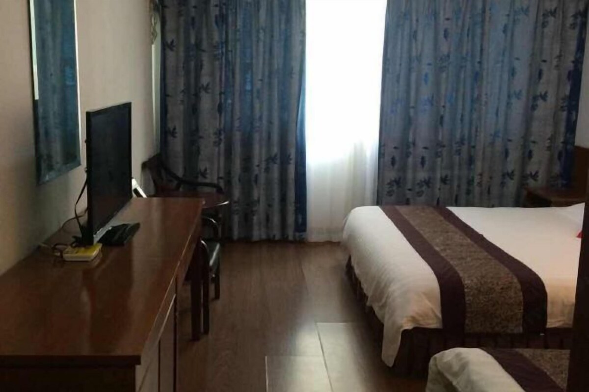 Una habitación de hotel con cama, escritorio con computadora y cortinas.