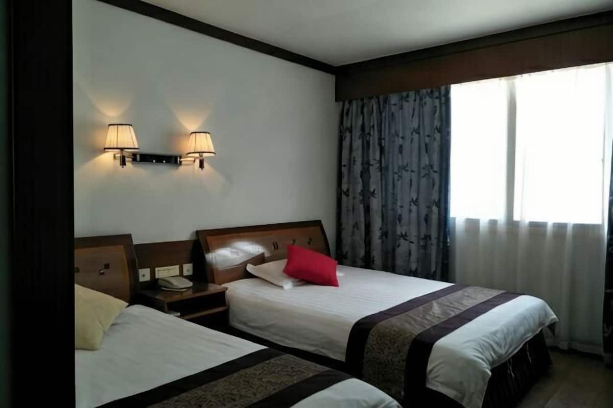 Una habitación de hotel con dos camas, una mesita de noche con lámpara y una ventana con cortinas.