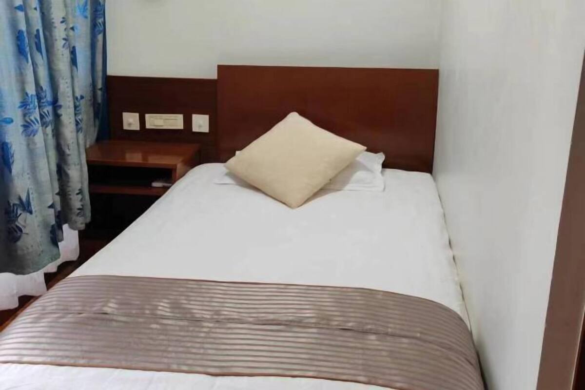Una cama bien hecha con cabecera de madera, una mesita de noche y una cortina con estampado floral.