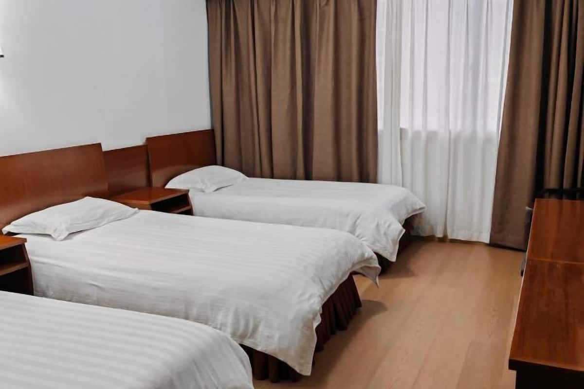 Habitación de hotel con tres camas individuales, cabeceros de madera, un escritorio de madera y una ventana con cortinas.