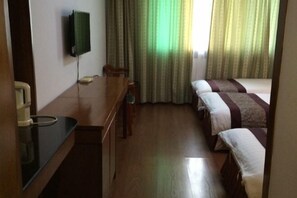 Una habitación de hotel con un escritorio de madera, un televisor montado en la pared, una cama con manta a rayas y una ventana con cortinas.