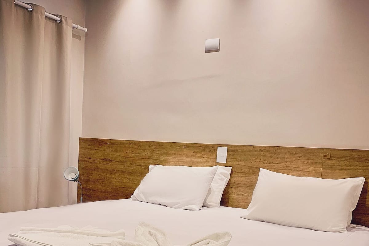 Ein Hotelzimmer mit einem ordentlich bezogenen Bett, einem Holzkopfteil und einem Badezimmer mit Duschvorhang.