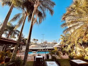 Un espace aménagé au bord de la piscine, avec des palmiers, des chaises longues et une piscine.