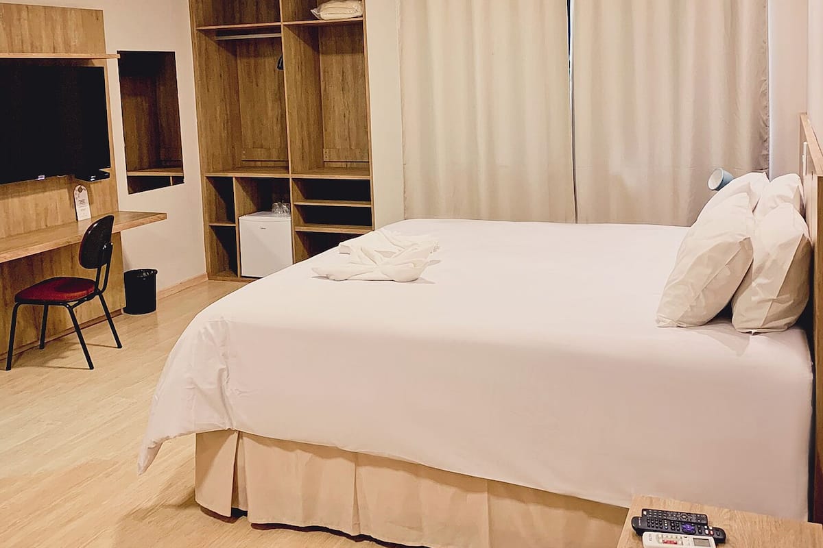 Ein Hotelzimmer mit einem Bett, einem Schreibtisch, einem Sessel, einem Fernseher, einem Kleiderschrank und einer Klimaanlage.
