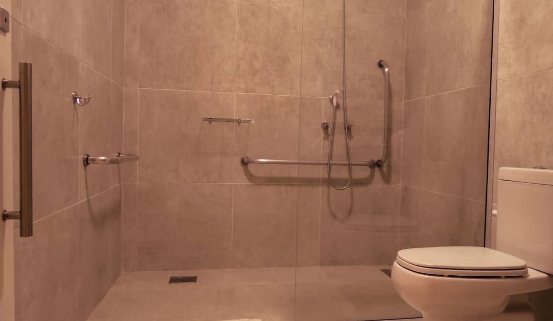 Een badkamer met douche, toilet en een greep.
