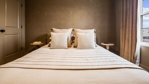 A neatly made bed with a striped bedspread, two pillows, and a bedside table with a book and a remote control. - The Winnie Lou (Jeffersonville)