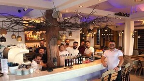 Zona de bar con un adorno central de árbol, taburetes y una barra con botellas.