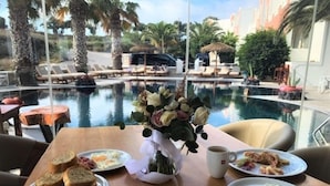 Una mesa de comedor con platos de desayuno, un jarrón de flores y vistas a una piscina y sillones de descanso.
