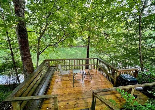 A wooden deck with a bench and chairs, surrounded by trees.