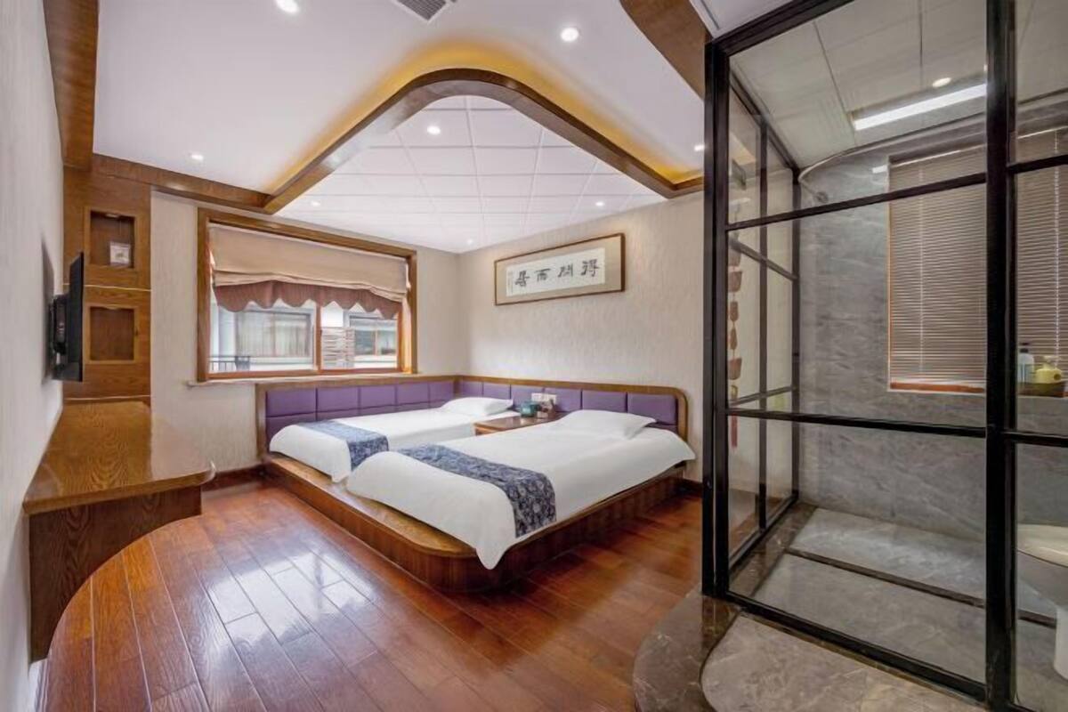 Une chambre d’hôtel avec un plancher en bois, deux lits, une télévision et une grande fenêtre.