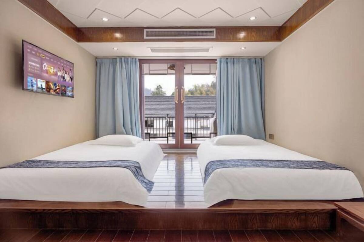 Une chambre d’hôtel avec deux lits, un téléviseur fixé au mur et un balcon avec vue.