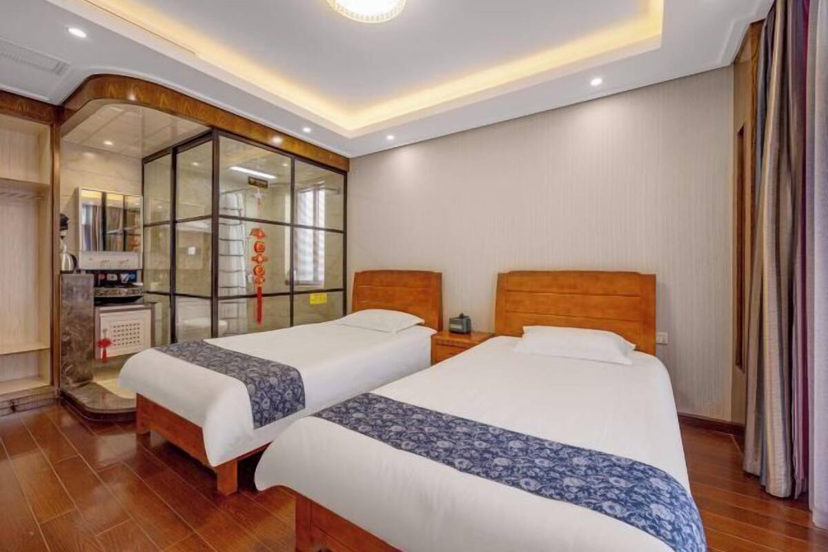 Une chambre d’hôtel avec deux lits, une tête de lit en bois, une cloison en verre et un petit bureau avec une chaise.