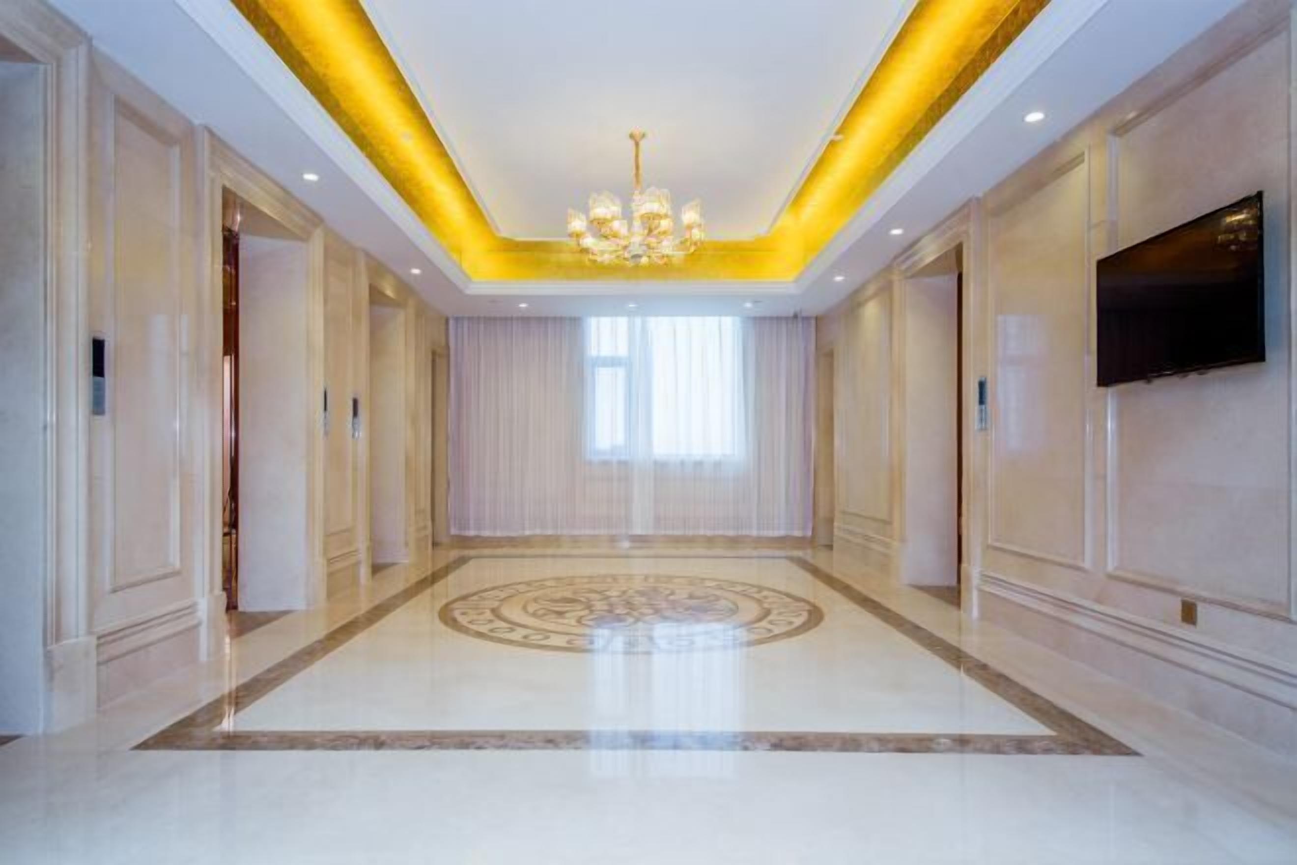 Un hall d’entrée spacieux, agrémenté d’un lustre, d’une grande fenêtre avec des rideaux et d’un téléviseur à écran plat fixé au mur.