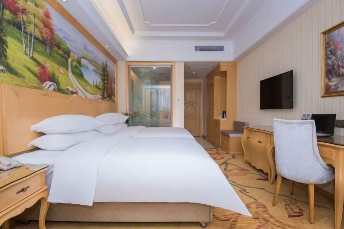 Habitación de hotel con una cama grande, un escritorio, una silla, un televisor y un cuadro en la pared.