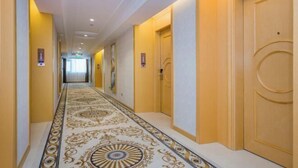 Un pasillo de hotel con alfombra estampada, puertas de madera e iluminación empotrada en el techo.