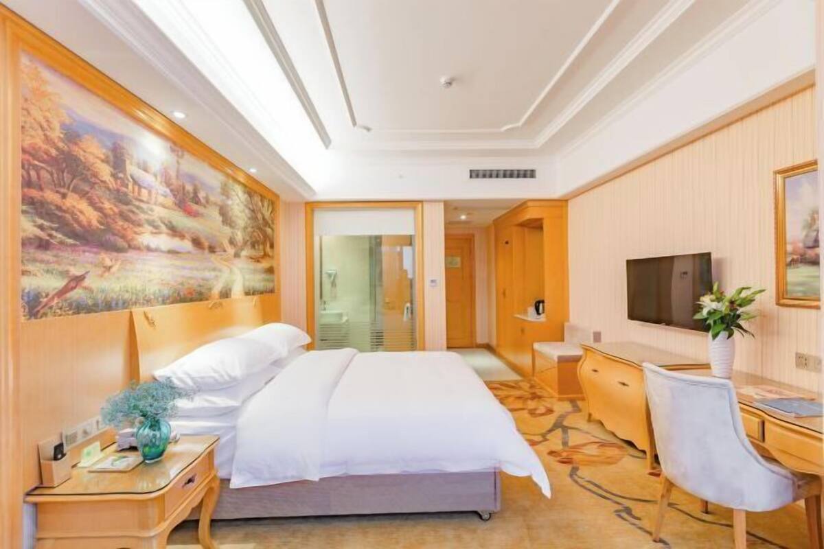 Una habitación de hotel con cama, escritorio, silla, televisor y un cuadro en la pared.
