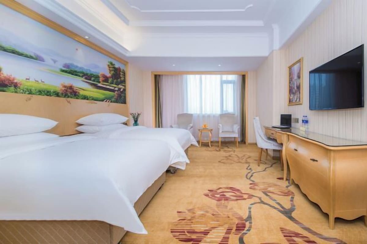 Une chambre d’hôtel avec un grand lit, un bureau, une chaise, une télévision et un tableau au mur.
