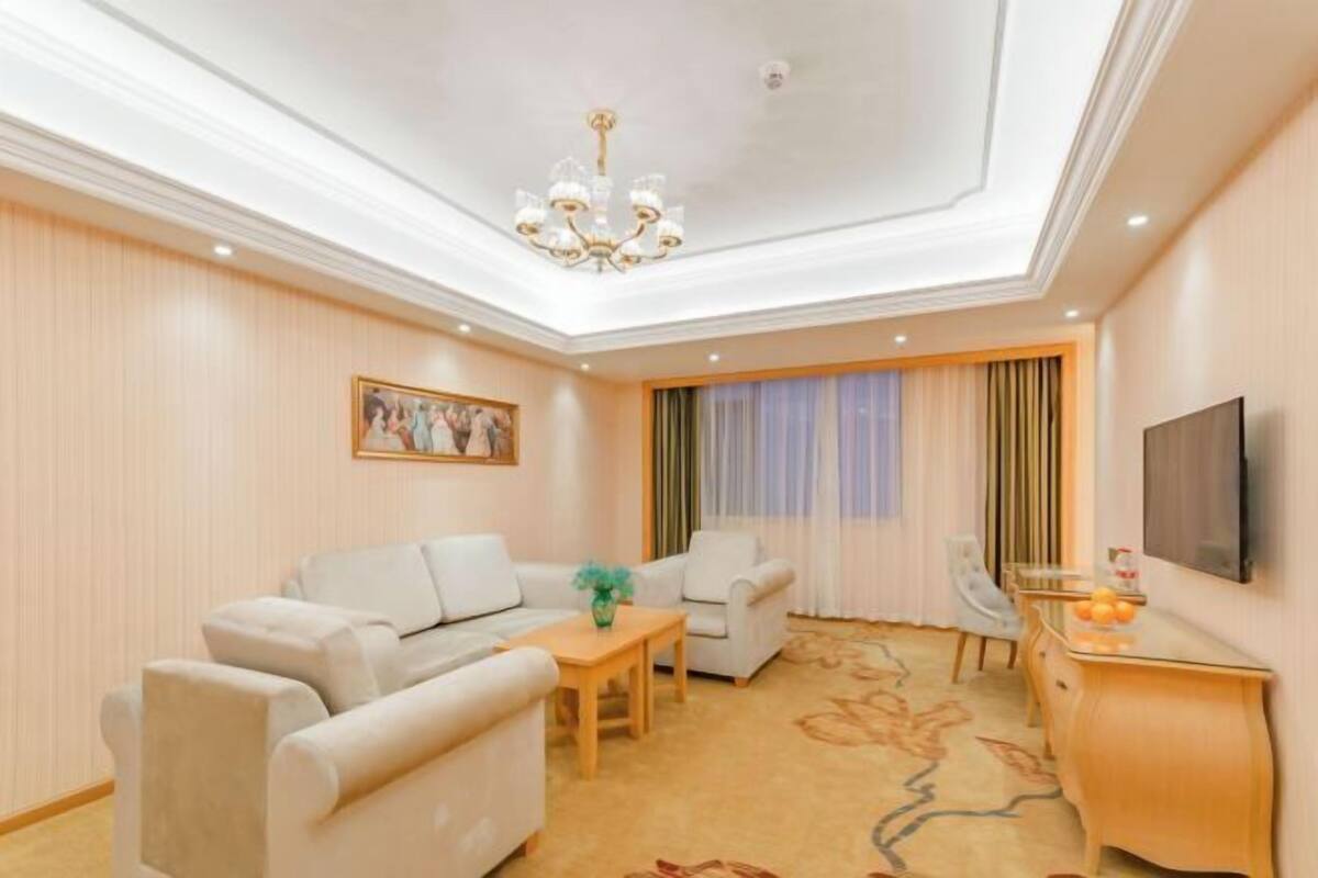 Habitación de hotel con un sofá, una mesa de comedor, un televisor y una araña.