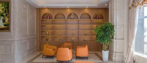A lobby with a marble floor, a reception desk, and a seating area with orange chairs.