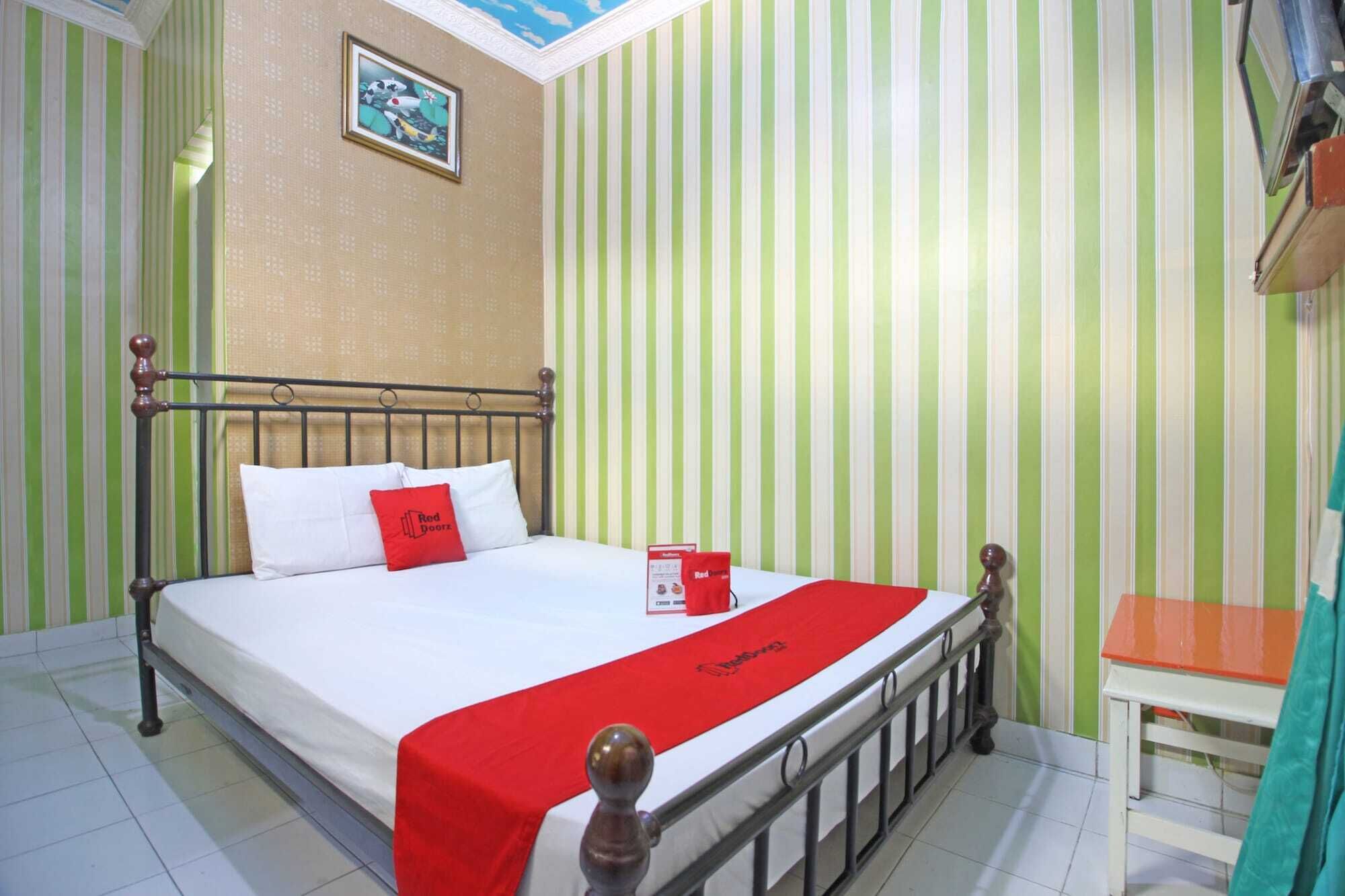Quarto de hotel com uma cama, um cobertor vermelho, um quadro na parede e papel de parede listrado.