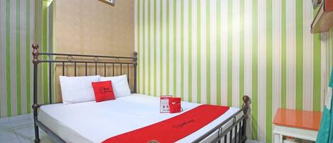 A hotel room with a bed, a red throw, a picture on the wall, and striped wallpaper.