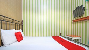 Habitación de hotel con cama, almohada roja, televisor montado en la pared y una pequeña mesa.