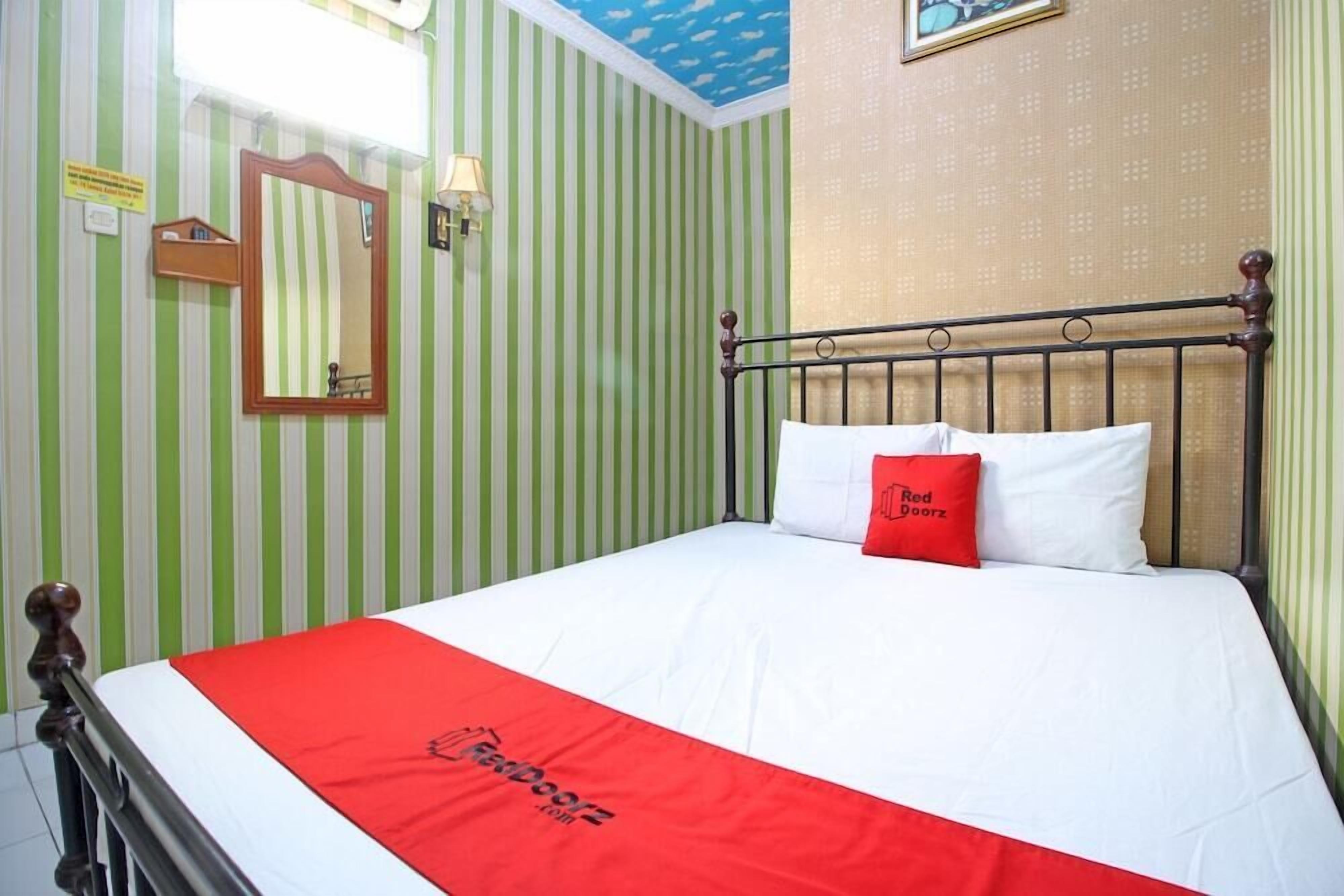 Une chambre d’hôtel avec un lit, une couvre-lit rouge et blanche, un oreiller rouge, un miroir et un papier peint à rayures.