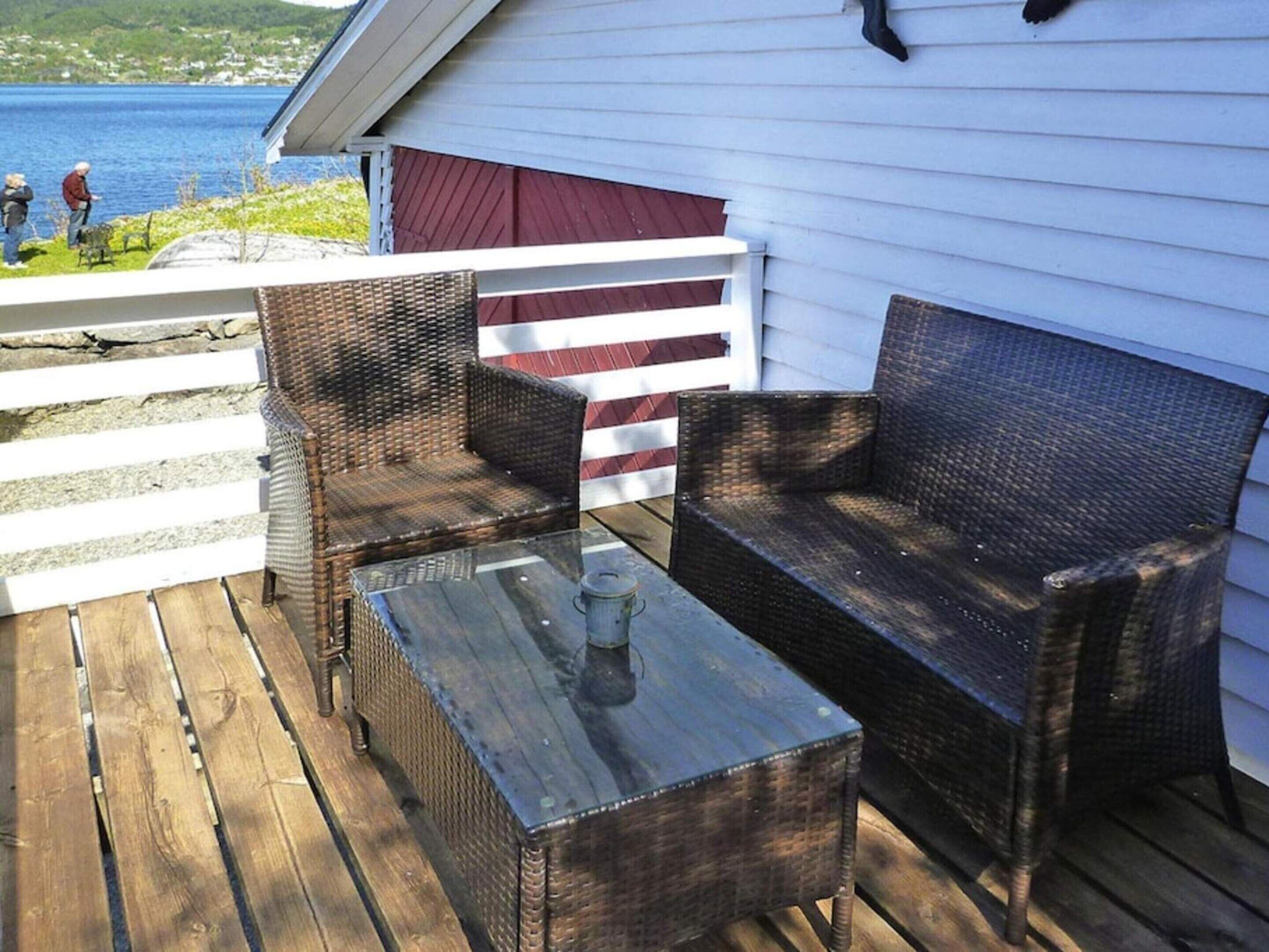 A wooden deck with wicker furniture and a glass table.