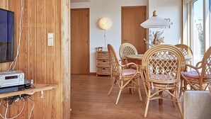 Une pièce avec un mur en bois, un coin repas avec des chaises en osier, une table et un luminaire suspendu.
