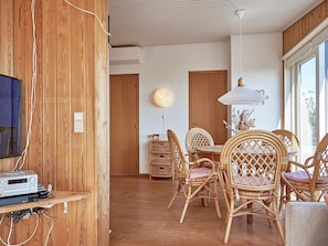 A room with a wooden wall, a dining area with wicker chairs, a table, and a hanging light fixture.