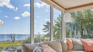 Un salon moderne doté d’une grande fenêtre donnant sur un plan d’eau et un espace verdoyant.