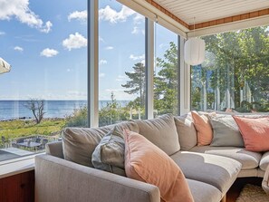 A modern living room with a large window overlooking a body of water and greenery.