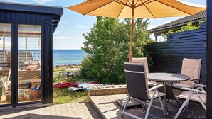 Une terrasse extérieure avec une table et des chaises, un grand parasol et une vue sur la mer.