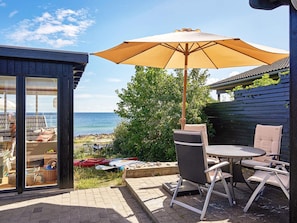 An outdoor patio with a table and chairs, a large umbrella, and a view of the sea.