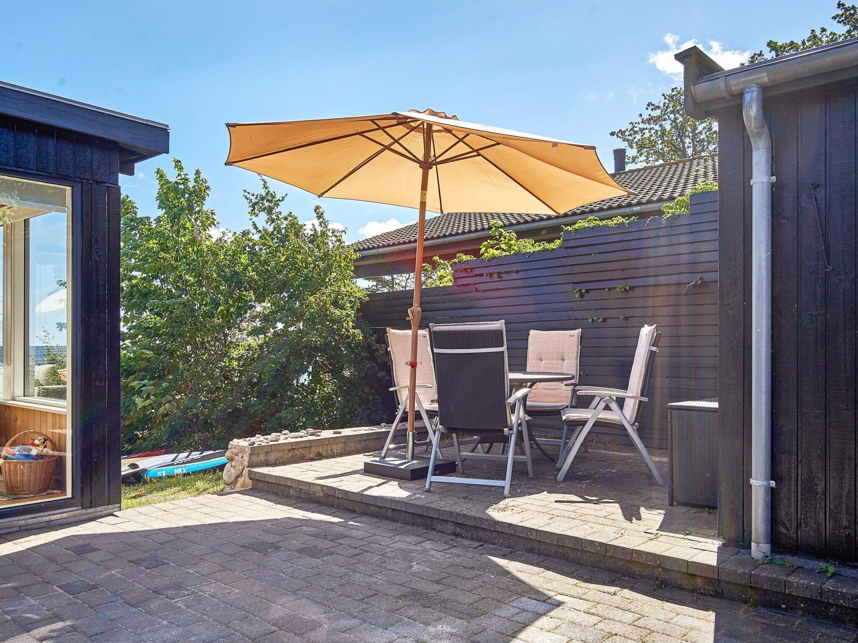 Une terrasse extérieure avec une table et des chaises, un grand parasol et une clôture en bois.