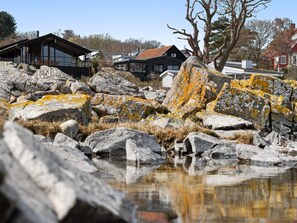 A lakeside property with large rocks, a wooden deck, and a house with large windows. - 4 Star Holiday Home in Allinge (Allinge)