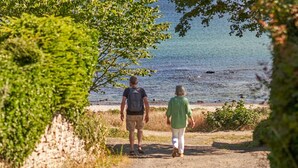 Deux personnes se promènent sur un sentier au bord d’une étendue d’eau, entourées de verdure.