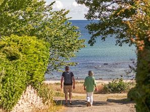 Two people walking on a path beside a body of water, surrounded by greenery.