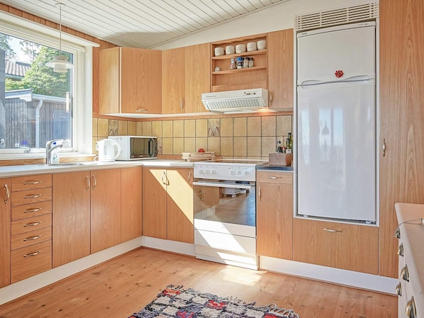 A compact kitchen with wooden cabinets, a white refrigerator, a microwave, and a stove.