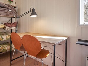 A study area with a desk, two chairs, a lamp, and a shelf with folded clothes.