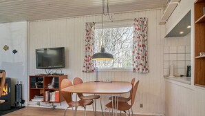 A cozy living room with a wooden table and chairs, a television, and a fireplace. - 4 Person Holiday Home in Aakirkeby (Akirkeby)