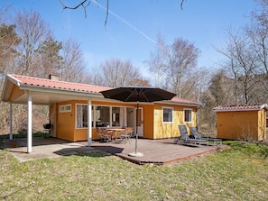 Eine Holzhütte mit überdachter Terrasse, Grillplatz und kleinem Gerätehaus.
