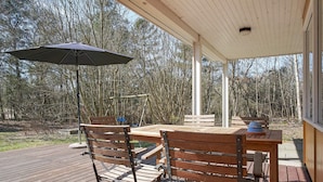 An outdoor wooden deck with a table and chairs, a blue umbrella, and a view of trees. - 4 Person Holiday Home in Aakirkeby (Akirkeby)