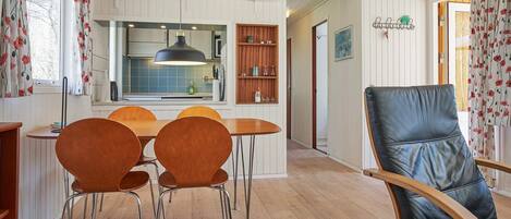 Un coin repas avec une table et des chaises en bois, un fauteuil en cuir noir et, au fond, une cuisine.