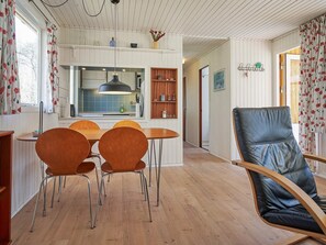 A dining area with a wooden table and chairs, a black leather chair, and a kitchen in the background. - 4 Person Holiday Home in Aakirkeby (Akirkeby)