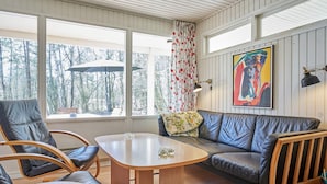 A cozy room with a wooden floor, a leather sofa, two leather chairs, a small wooden table, and a window with a view of trees. - 4 Person Holiday Home in Aakirkeby (Akirkeby)