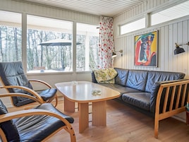 Un cuarto acogedor con piso de madera, un sofá de cuero, dos sillones de cuero, una mesita de madera y una ventana con vista a árboles.